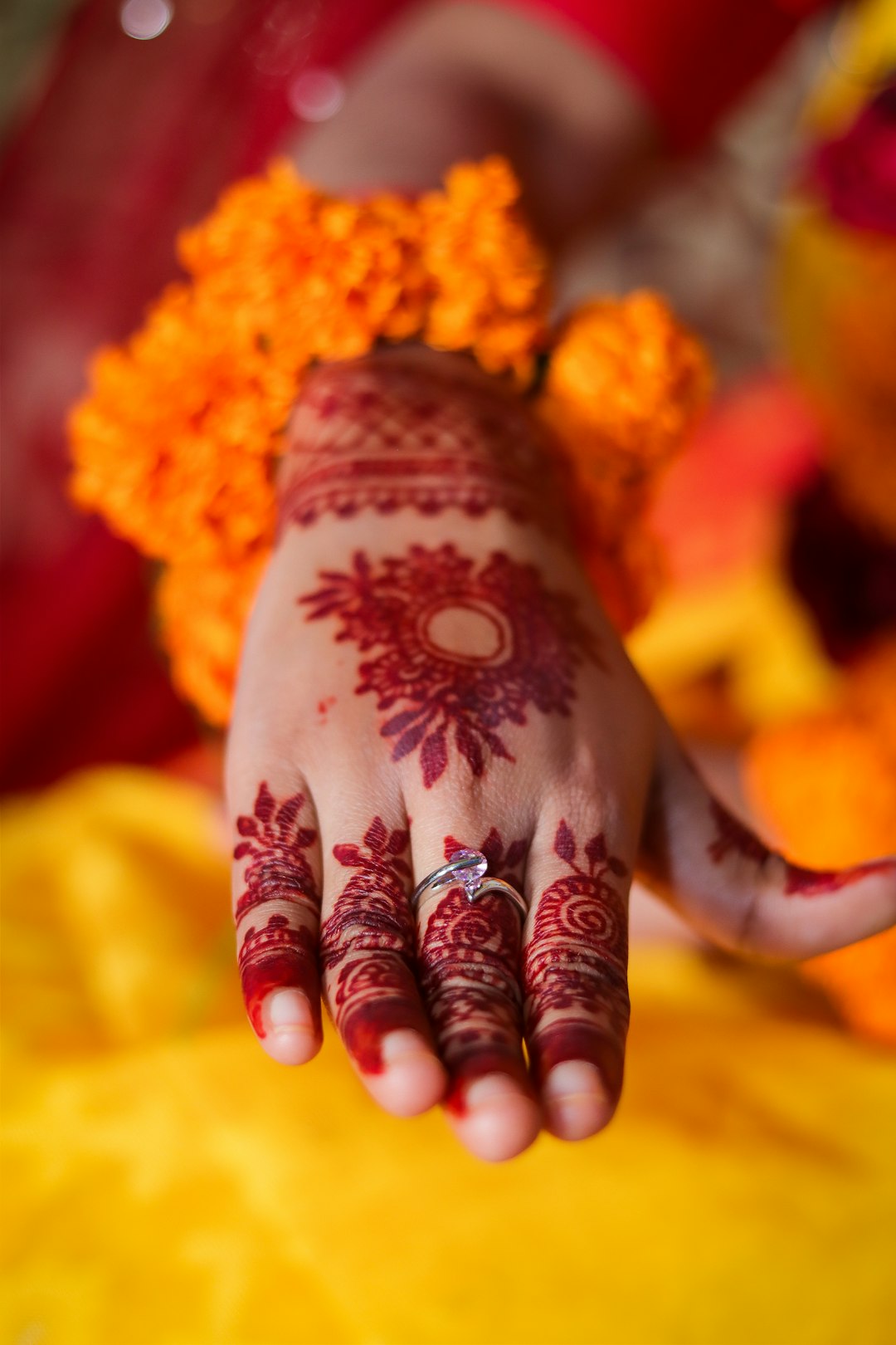 Bridal Mehndi Hands with Marigold Floral Bangles on Yellow Saree. Close-up of a bride’s hands adorned with intricate mehndi (henna) designs during a traditional pre-wedding ceremony. The hands rest gracefully on a vibrant yellow saree, decorated with