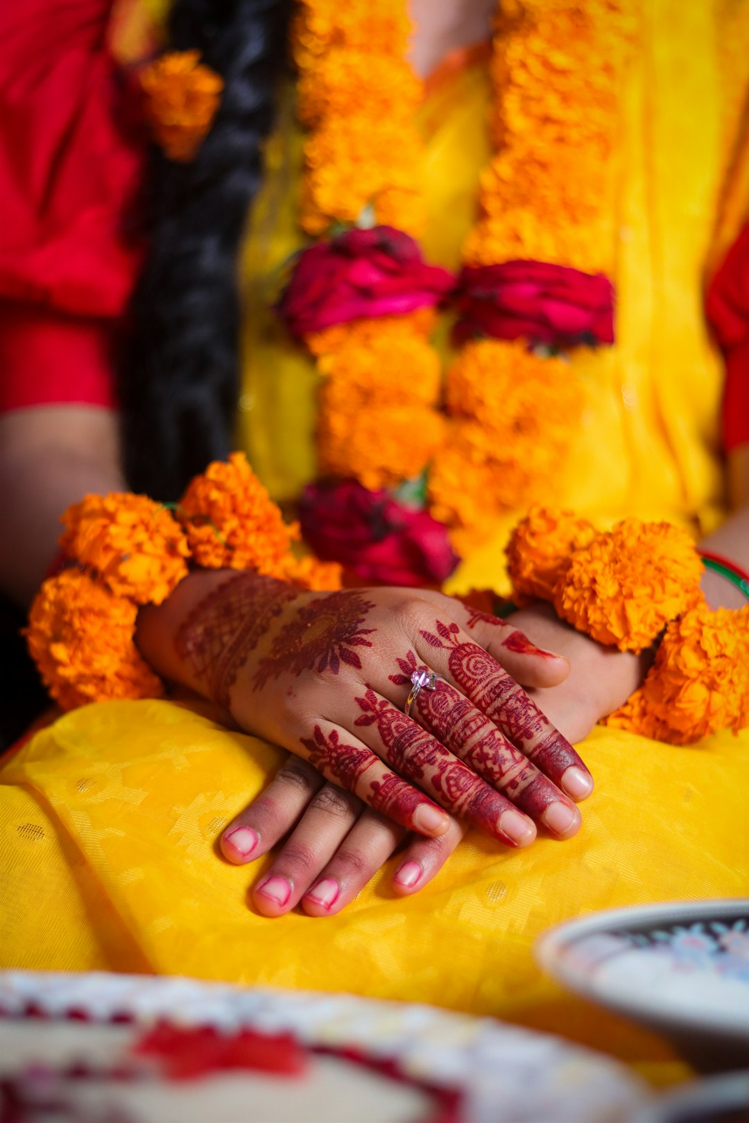 Bridal Mehndi Hands with Marigold Floral Bangles on Yellow Saree. Close-up of a bride’s hands adorned with intricate mehndi (henna) designs during a traditional pre-wedding ceremony. The hands rest gracefully on a vibrant yellow saree, decorated with