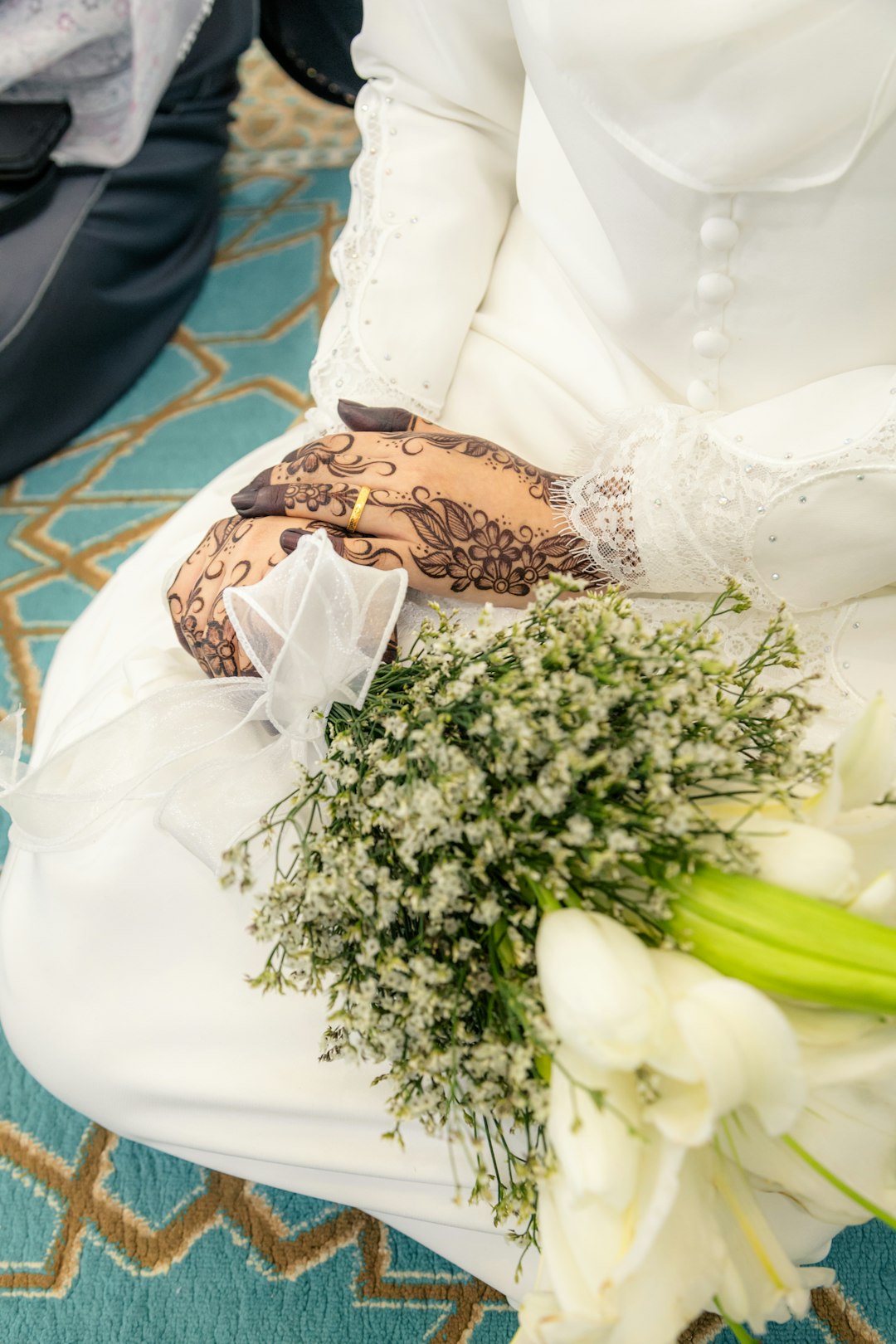 Bride's hands with henna and wedding ring holding bouquet.