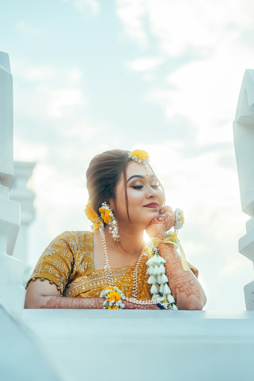 Woman in traditional attire with floral jewelry under bright sky.
