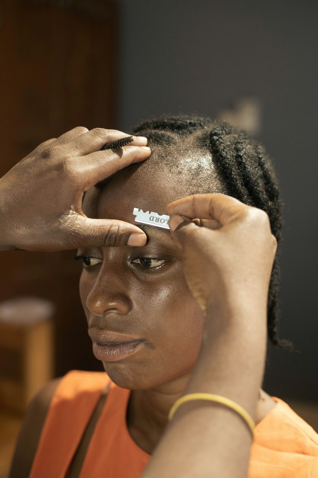 Hands groom a woman's eyebrow with a styling tool.