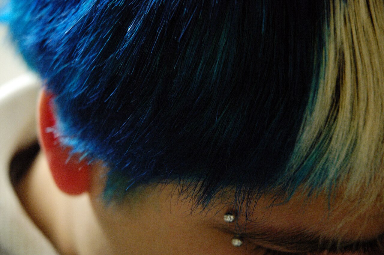 Person with blue hair and eyebrow piercing.