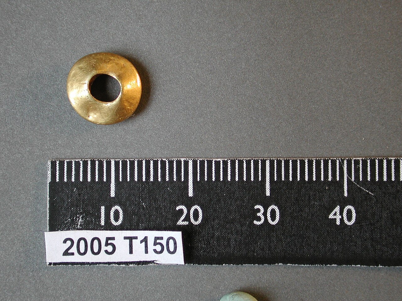 Complete, annular sheet gold bead. The bead has a flattened hexagonal section, having bevelled sides to top and bottom and is hollow. It has a circular piercing. The bead is undecorated. It dates from