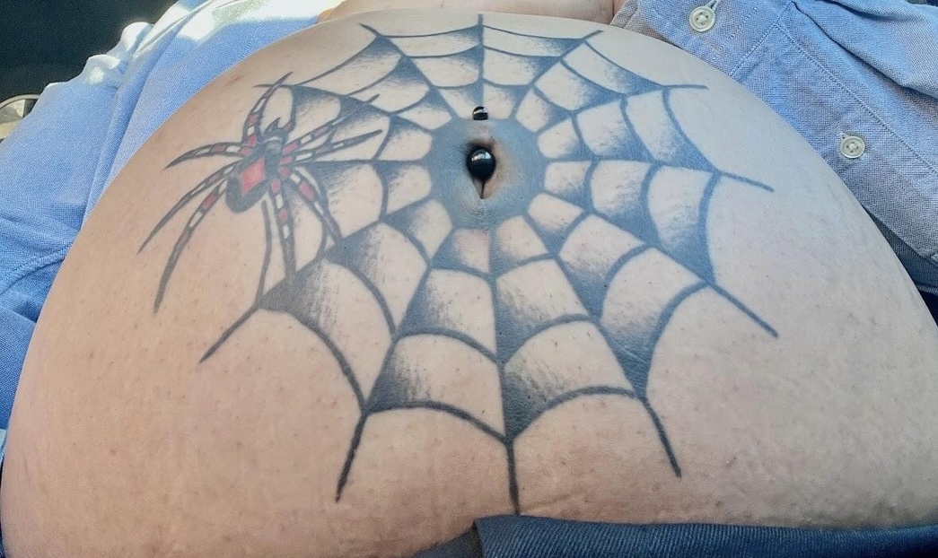 A person’s tattooed belly of a spiderweb and piercing