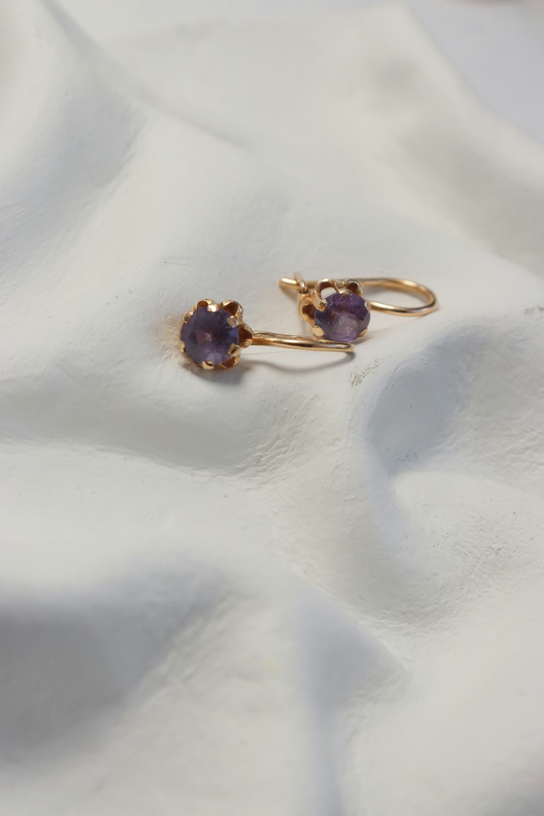 Amethyst earrings rest on a white, silky fabric.