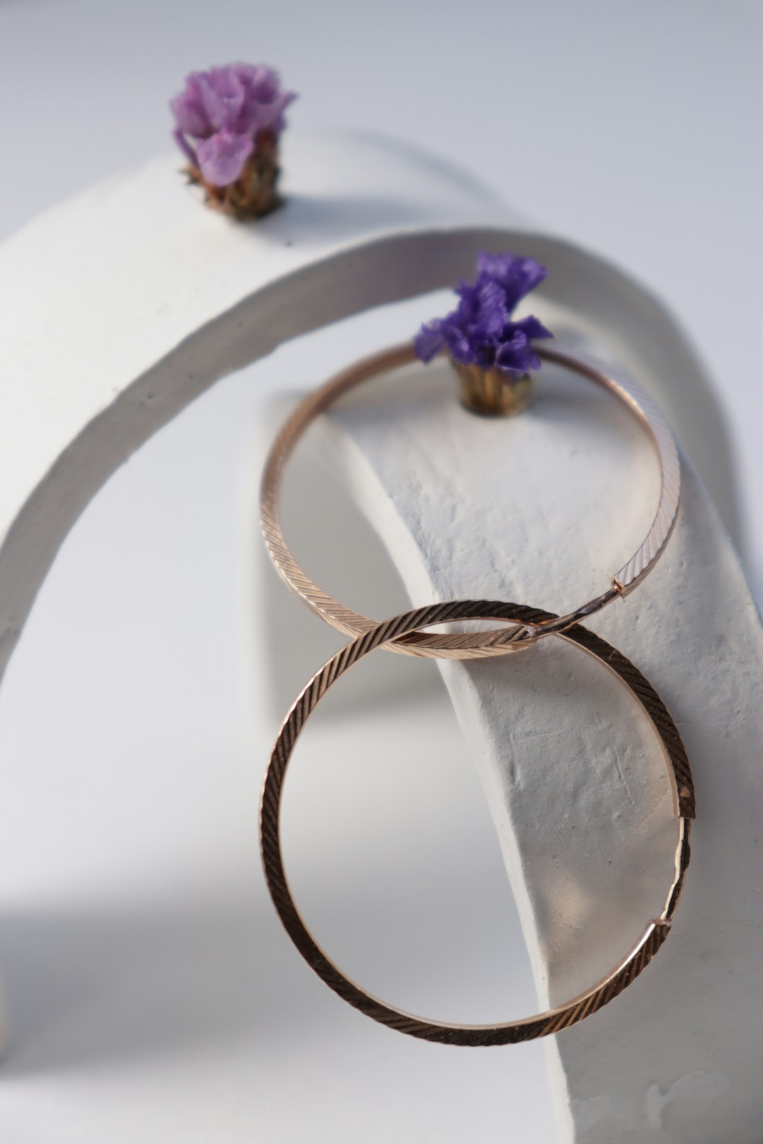 Golden hoop earrings are displayed with pretty flowers.