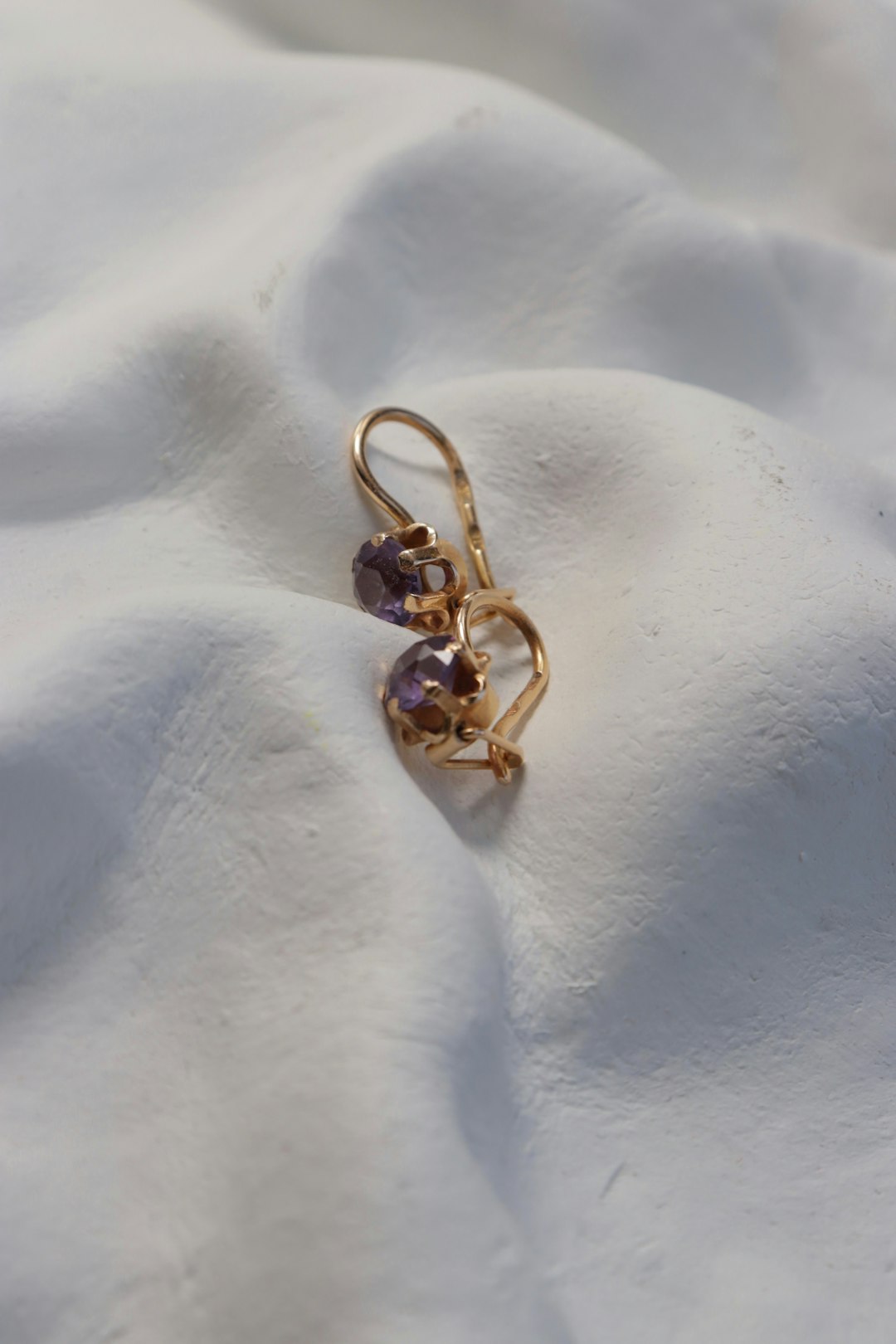 Golden earrings with purple gemstones on white surface.