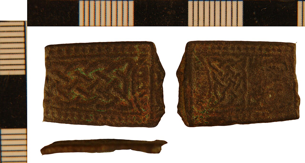 Copper alloyStrap End fragment. Cast tapered plate fragment with trace of bifurcation at its broken wider end, probably from a tongue shaped strap end - the other end is also lost. A design of strap-