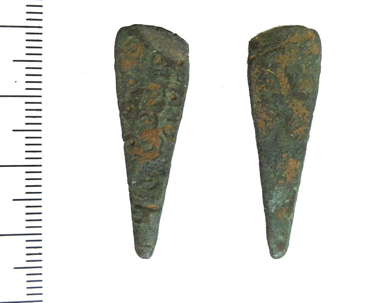 A late Saxon copper-alloy strap-end. The strap-end is tongue-shaped and damaged at the bifurcated attachment-end. The upper-side of the body is decorated with rows of punched ring and dot motifs. The