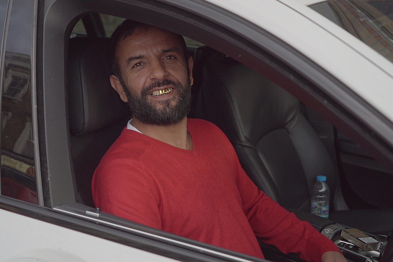 A Kashmiri man shows off his gold teeth as he drives through South London